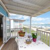 Terrazza con vista sul mare, tavolo apparecchiato e fiori, spiaggia con ombrelloni bianchi.