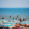 Ombrelloni colorati su una spiaggia, bagnanti in mare azzurro.