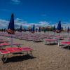 Spiaggia con lettini rossi e ombrelloni blu sotto un cielo sereno.