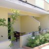 Ingresso di una casa color crema con piante verdi e una piccola veranda.