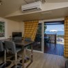 Sala con tavolo alto, sedie grigie e vista mare attraverso porta finestra aperta.