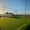 Campo da calcio in erba con rete, tende in lontananza e mare al tramonto.
